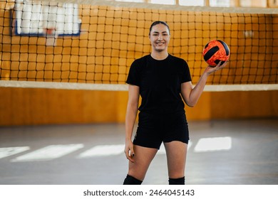 Portrait of a female professional volleyball player in action playing a match in a sports hall. Woman standing on a volleyball court with a ball in her hands and posing while looking at the camera. - Powered by Shutterstock