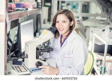 Portrait of a female researcher working in a lab scientist using microscope with colleague working in Background