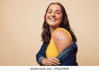 Porträt eines weiblichen Lächelns nach einer Impfung. Frauen halten ihre Hemdärmel niedrig und zeigen ihren Arm mit Verband nach Impfung.