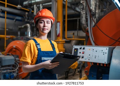 Portrait of female smiling worker in uniform and helmet with a folder and a pen in her hand. In the background-boiler room.