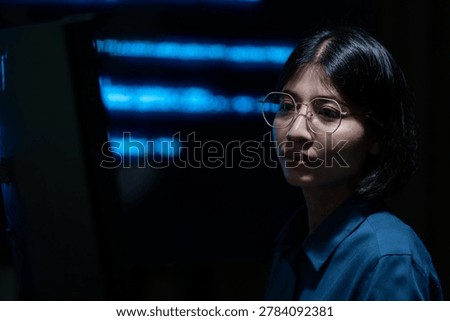 Portrait of a female software developer in a dark office environment with illuminated digital technology screens in the background. The image represents cybersecurity, software engineering, and modern information technology concepts.