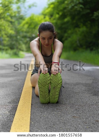 Portrait of female in sport ware stretching legs to touch her toe after morning run in nature