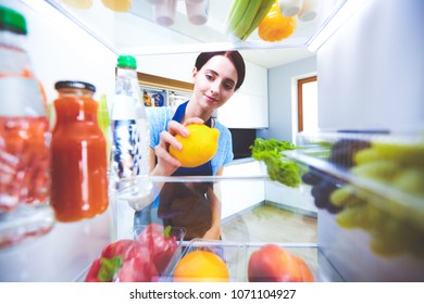 Portrait of female standing near open fridge full of healthy food, vegetables and fruits. Portrait of female - Shutterstock ID 1071104927