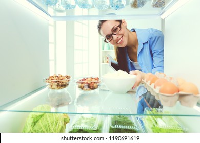 Portrait Of Female Standing Near Open Fridge Full Of Healthy Food, Vegetables And Fruits.