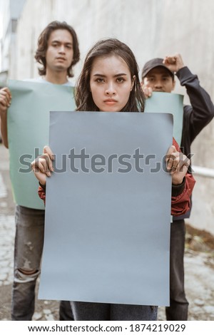 Portrait female students demonstrating with their friends holding blank paper