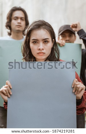 Portrait female students demonstrating with their friends holding blank paper