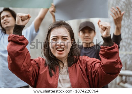 Portrait female students demonstrating with their friends holding blank paper in the background