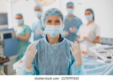 Portrait of female surgeon in mask and gloves standing in operating room, ready to work on patient - Powered by Shutterstock