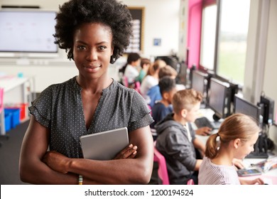 Portrait Of Female Teacher Holding Digital Tablet Teaching Line Of High School Students Sitting By Screens In Computer Class