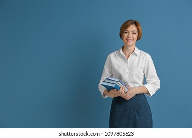 Portrait Of Female Teacher With Notebooks On Color Background