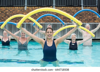 Portrait of female trainer and senior swimmers exercising with pool noodle - Powered by Shutterstock