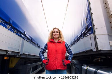 Portrait of female trucker proudly standing between trailers and truck vehicle. Transportation service.
