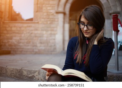 Portrait of a female university student reading interesting book on campus, charming teenager sitting outdoors with open book, attractive young girl read absorbing book, flare light, filtered image - Powered by Shutterstock