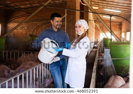 Portrait of female veterinarian and male farmer talking about all-mash forage for animals in pigsty