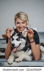 Portrait Of Female Veterinarian Specialist Holding Ears Of Purebred Siberian Husky Dog.