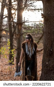 Portrait Of A Female Viking Standing In The Forest With An Axe. She Is Wearing Fur And Has Her Hair In Braids. The Sun Is Setting. 