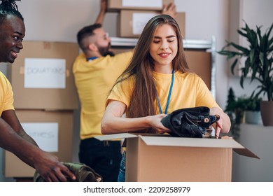 Portrait of a female volunteer packing clothes donation. Diverse people working in charitable foundation. Happy woman separating donation stuff. Volunteers sort donations during food drive. - Powered by Shutterstock