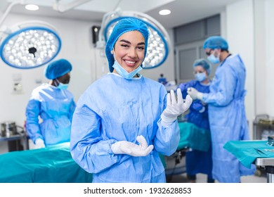 Portrait of female woman nurse surgeon OR staff member dressed in surgical scrubs gown mask and hair net in hospital operating room theater making eye contact smiling pleased happy looking at camera
