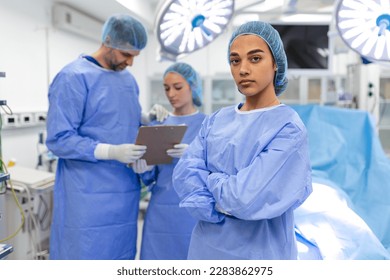 Portrait of female woman nurse surgeon OR staff member dressed in surgical scrubs gown mask and hair net in hospital operating room theater making eye contact smiling pleased happy looking at camera