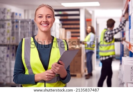 Portrait Of Female Worker Inside Busy Warehouse Checking Stock On Shelves Using Digital Tablet
