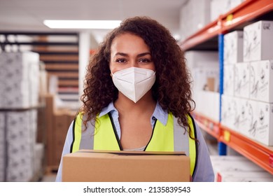 Portrait Of Female Worker Wearing PPE Face Mask Holding Box Inside Warehouse