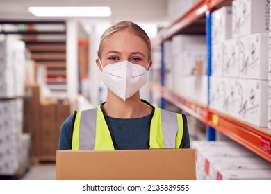 Portrait Of Female Worker Wearing PPE Face Mask Holding Box Inside Warehouse