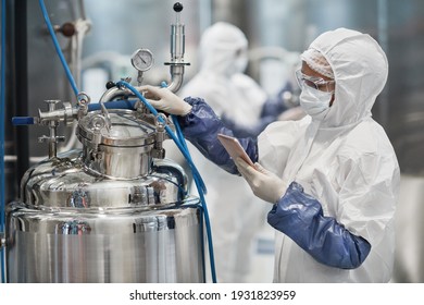Portrait of female worker wearing protective suit while operating equipment at modern chemical plant, copy space