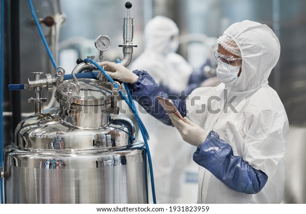 Portrait of female\
worker wearing protective suit while operating equipment at modern\
chemical plant, copy\
space