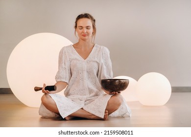 Portrait of a female yoga teacher playing a Tibetan bowl or singing a bell in the gym during a yoga retreat.