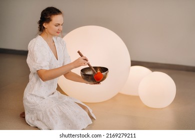 Portrait Of A Female Yoga Teacher Playing A Tibetan Bowl Or Singing A Bell In The Gym During A Yoga Retreat.