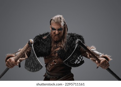 Portrait of fierce viking from past with dual axes against gray background.