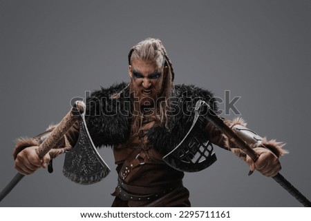 Portrait of fierce viking from past with dual axes against gray background.