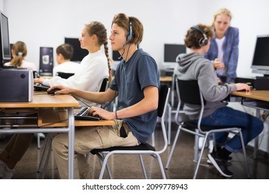 Portrait of a fifteen-year-old schoolboy in headphones, studying at a computer in the classroom at a informatics lesson