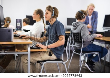 Portrait of a fifteen-year-old schoolboy in headphones, studying at a computer in the classroom at a informatics lesson