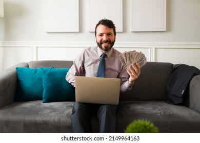 Portrait Of A Financially Stable Man Smiling While Showing A Lot Of Money And Using His Online Bank On The Laptop