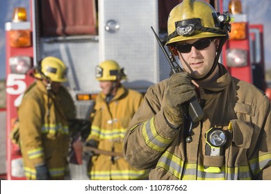 Portrait of a firefighter talking on radio with colleagues standing in the background - Powered by Shutterstock