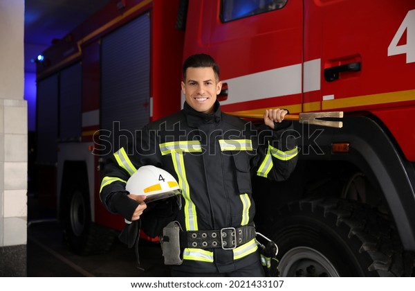 Portrait of firefighter in uniform with
helmet and entry tool near fire truck at
station