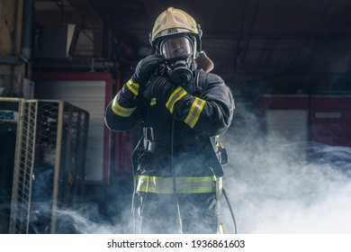 Portrait of a fireman wearing firefighter turnouts and helmet. Dark background with smoke and blue light.