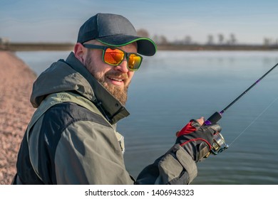 Portrait of fisherman. Bearded man in cap and sunglasses holds fishing rod at lake - Powered by Shutterstock