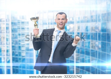 Portrait of fists gesturing businessman with gold cup, blue background