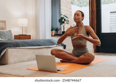 Portrait of fit African American woman practicing breathing, having online training, using laptop sitting on mat at home. Healthy lifestyle, sport concept - Powered by Shutterstock