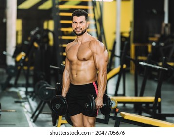 Portrait of a fit caucasian man holding dumbbells while standing in a gym