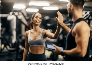 Portrait of a fit happy sportswoman giving high five to her coach in a gym. Gym workout. Fitness trainer.