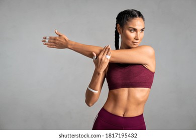 Portrait of fit middle aged woman doing arm stretching isolated on grey background. Determined latin woman warming up before training on gray background with copy space. Woman doing fitness exercise.