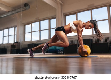 Portrait of a fit and muscular woman doing intense core workout with kettlebell in gym. Female exercising at crossfit gym.