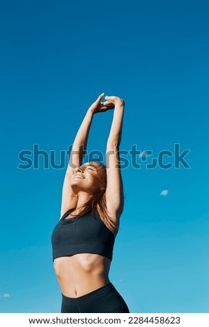 Portrait of a fit smiling beautiful girl stretching and deep breathing in front of a clear blue sky in a summer windy sunny day