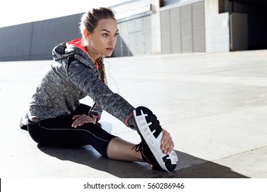 Portrait of fit and sporty young woman doing stretching in city.