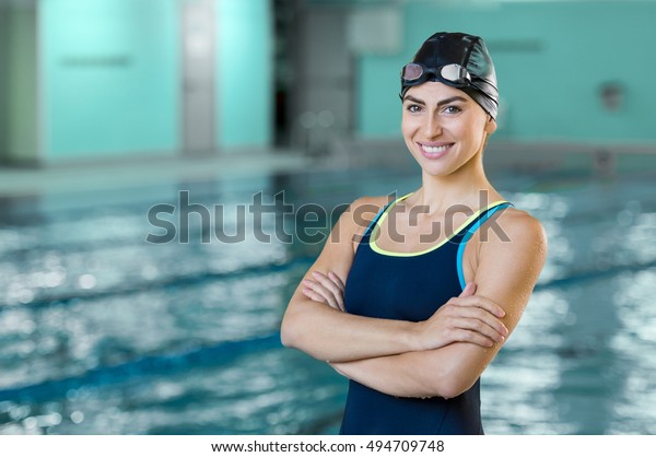 カメラを見ながらプールにいるフィットした泳ぎ手の女性のポートレート 競泳プール近くの競泳女性 のポートレート プールサイドで泳ぎ帽と交差した腕を持つゴーグルをかぶった若い水泳選手 の写真素材 今すぐ編集