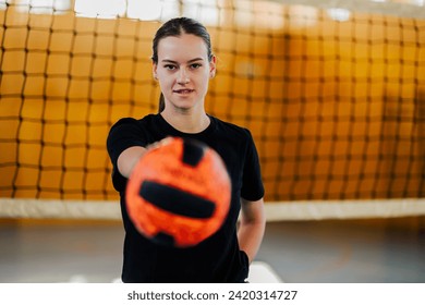 Portrait of a fit teenage sportswoman standing on volleyball court with a ball and showing it to the camera. A young volleyball player is standing with a ball her hand on volleyball court. Copy space. - Powered by Shutterstock