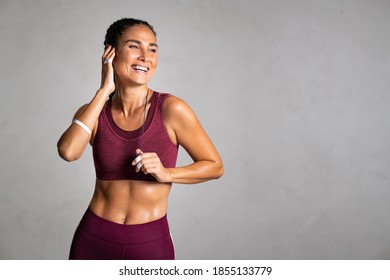 Portrait of fit woman smiling while listenig music with wireless headphones. Laughing fitness middle aged woman with perfect body relaxing after gym training on grey background wall with copy space. - Powered by Shutterstock
